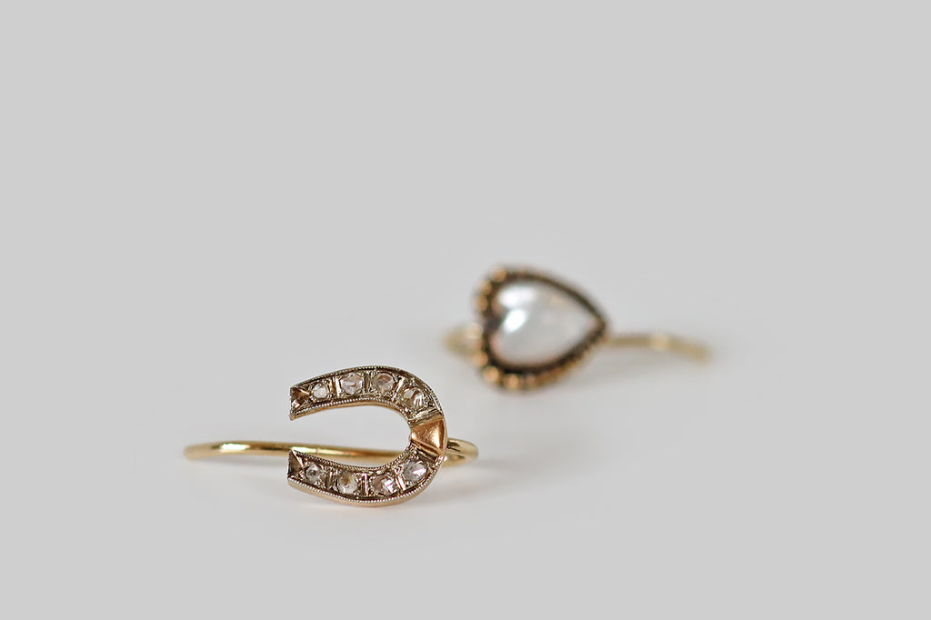 Antique Jewelry Portland, Vintage Jewelry Portland , Antique Engagement Rings | Poor Mouchette | A dainty pair of mismatched drop earrings whose subjects, a lucky horseshoe and a moonstone heart, rest on the wearer's earlobe. The tiny horseshoe, here, is faced with platinum and is set with eight, glinting rose cut diamonds.