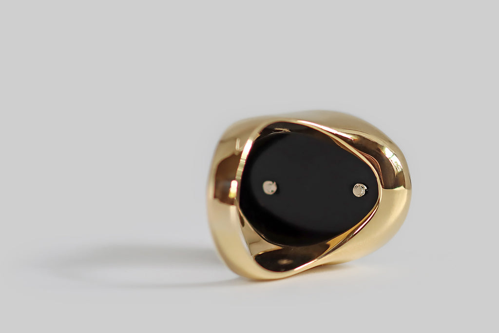 Antique Jewelry Portland, Vintage Jewelry Portland , Antique Engagement Rings | Poor Mouchette | A big, Art Deco era signet ring, modeled in 18k yellow gold, whose oval face is set with a polished slab of black onyx. This glassy onyx gem has straight sides that stand slightly proud of the ring's smooth, integral bezel. Atop the onyx, a bold, curvaceous, white-gold fleur de lis is mounted, with rivets.
