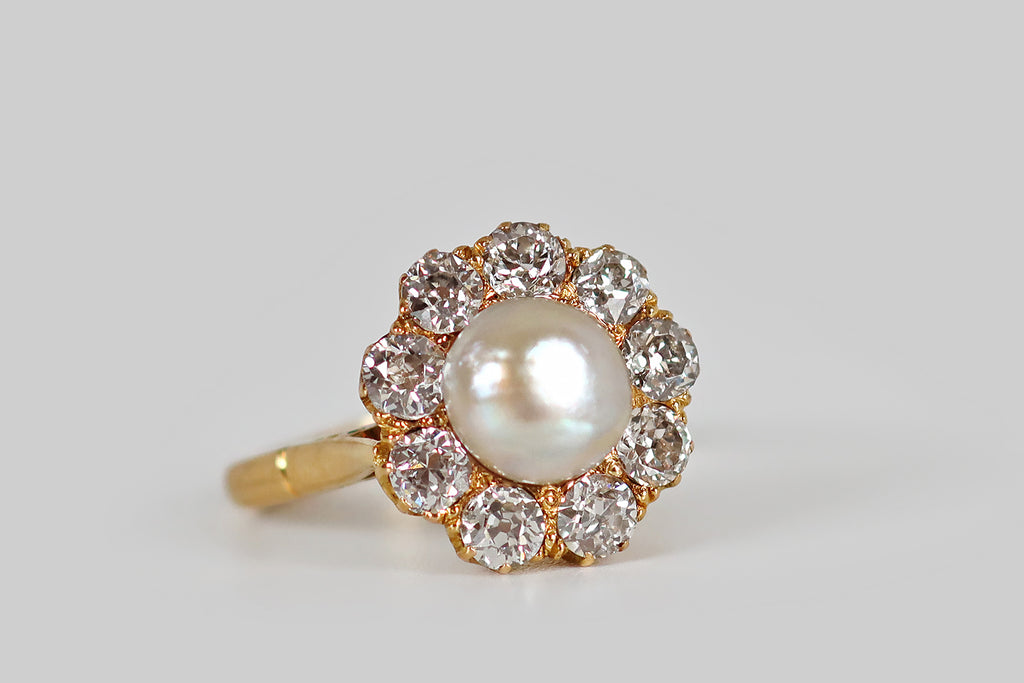 Antique Jewelry Portland, Vintage Jewelry Portland , Antique Engagement Rings | Poor Mouchette | An early 20th century cluster ring, modeled in 18k yellow gold, whose central gem is an especially lustrous natural sea pearl. This large, white, button pearl has glowy, iridescent nacre. It is mounted in a closed-back seat, where it is surrounded by a halo of nine old European cut diamonds (approx 1.45 ctw). 
