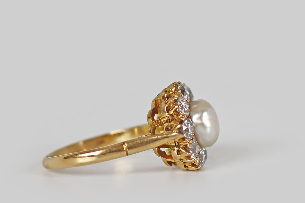 Antique Jewelry Portland, Vintage Jewelry Portland , Antique Engagement Rings | Poor Mouchette | An early 20th century cluster ring, modeled in 18k yellow gold, whose central gem is an especially lustrous natural sea pearl. This large, white, button pearl has glowy, iridescent nacre. It is mounted in a closed-back seat, where it is surrounded by a halo of nine old European cut diamonds (approx 1.45 ctw). 