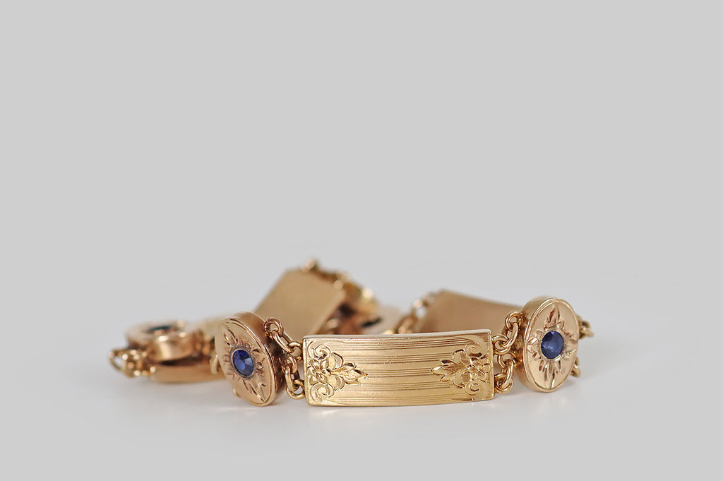Antique Jewelry Portland, Vintage Jewelry Portland , Antique Engagement Rings | Poor Mouchette | A charming, antique Arts &amp; Crafts panel bracelet, hand fabricated in 14k rosy yellow gold. Composed of five rectangular plaques, and five oval stations, this bracelet features fine, repeating hand-engraved details— flower finials that lay atop pinstriped fields, and flaming stars, flush-set with faceted (old cut) cornflower-blue sapphires. 