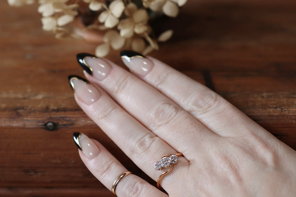 Poor Mouchette | Curated Antique Jewelry, Vintage Jewelry & Engagement Rings | Portland, Oregon | An elegant, Edwardian-era engagement ring, modeled in 22k yellow gold and platinum, whose modified bypass style cradles a trio of old cut diamonds (a central old mine cut, and a flanking pair of old Euros). This ring is styled with slim, curving, symmetrical shoulders that become part of the ring face— the shapely wires read like cupped hands, reaching out to hold the ring's three hand-cut diamonds.