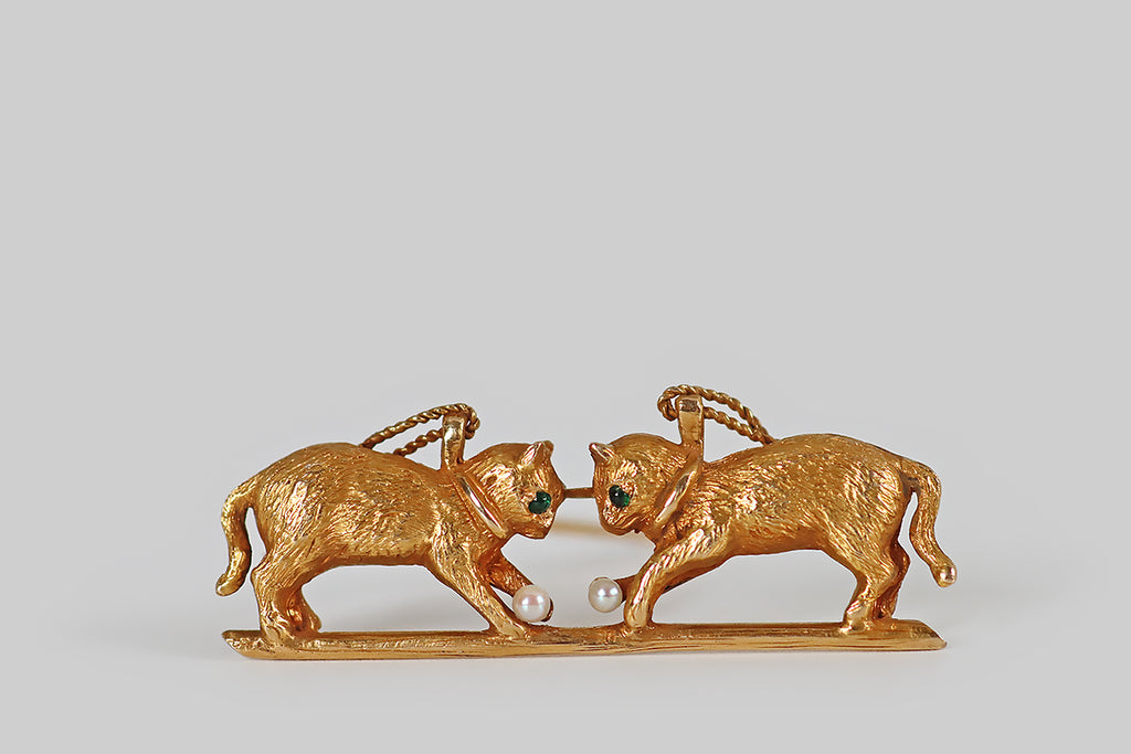 Antique Jewelry Portland, Vintage Jewelry Portland , Antique Engagement Rings | Poor Mouchette | A charming Edwardian-era novelty brooch, modeled substantially in 14k yellow gold, which depicts a pair of kitties at play! These sweet cats are realistically rendered in three dimensions, with beautifully-textured fur details, and emerald cabochon eyes; each cat wears a little collar and a twisted wire leash. Our feline friends are nearly symmetrical