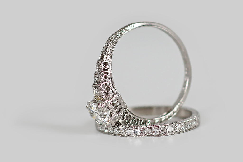 Poor Mouchette | Curated Antique Jewelry, Vintage Jewelry & Engagement Rings | Portland, Oregon | A charming 1920s wedding set, modeled in platinum, whose engagement ring features an especially pretty 1/2 carat transitional cut diamond (F/G, VVS). This sparkling, hand-cut diamond is mounted in an open, square-ish, "picture-corner" style basket, where single beads further secure it, in each of the basket's four corners. Alongside this primary diamond, trios of diamonds, set into square, stepped seats