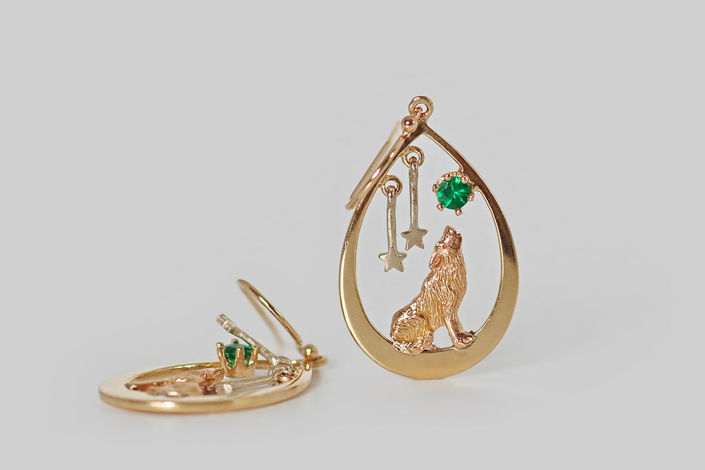 Poor Mouchette | Curated Antique Jewelry, Vintage Jewelry & Engagement Rings | Portland, Oregon | A very cool pair of late-vintage dangling earrings, modeled in 14k gold, whose open, teardrop-shaped form is home to a wolf, an emerald "moon," and a pair of white gold stars. Our beautiful wolf howls at this green moon, which is set in a six prong basket, while the stars drop and sway freely over their left shoulder. 