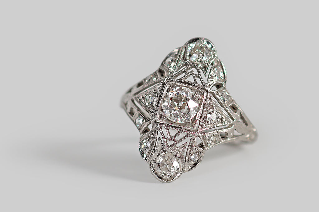 Poor Mouchette | Curated Antique Jewelry, Vintage Jewelry & Engagement Rings | Portland, Oregon | An elegant Art Deco era ring, modeled in platinum, whose low-profile, shield-like face has a delicate, lacy perimeter. This intricate old darling is hand-pierced and engraved, with a combination of geometric and floral elements, and it is set with a clutch of sparkling old European cut diamonds.