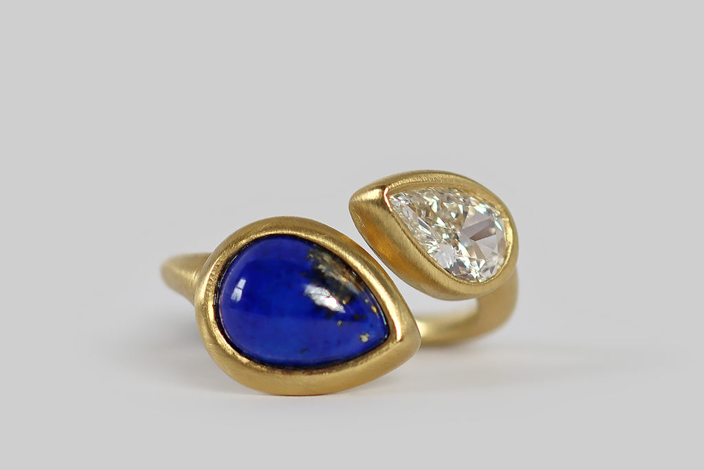 Poor Mouchette | Curated Antique Jewelry, Vintage Jewelry & Engagement Rings | A striking contemporary toi et moi ring, modeled in 18k yellow gold, whose gems are a .70 carat, pear-shaped diamond (G/H, VS), and a vibrant, gold-flecked, lapis lazuli cabochon (also pear-shaped). The pyrite figuring in this lapis gem is heavy and especially fine, reading like a splash on one side. The 9 mm diamond has a big presence on the hand; it is sparkling, near-colorless and beautifully cut.