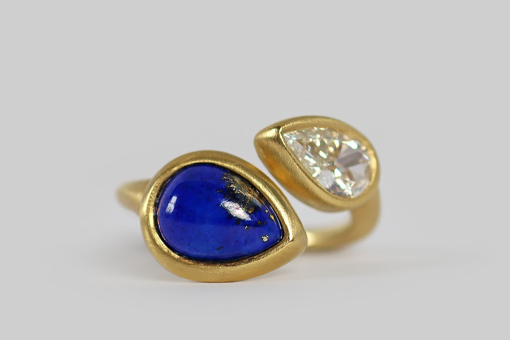 Poor Mouchette | Curated Antique Jewelry, Vintage Jewelry & Engagement Rings | A striking contemporary toi et moi ring, modeled in 18k yellow gold, whose gems are a .70 carat, pear-shaped diamond (G/H, VS), and a vibrant, gold-flecked, lapis lazuli cabochon (also pear-shaped). The pyrite figuring in this lapis gem is heavy and especially fine, reading like a splash on one side. The 9 mm diamond has a big presence on the hand; it is sparkling, near-colorless and beautifully cut.