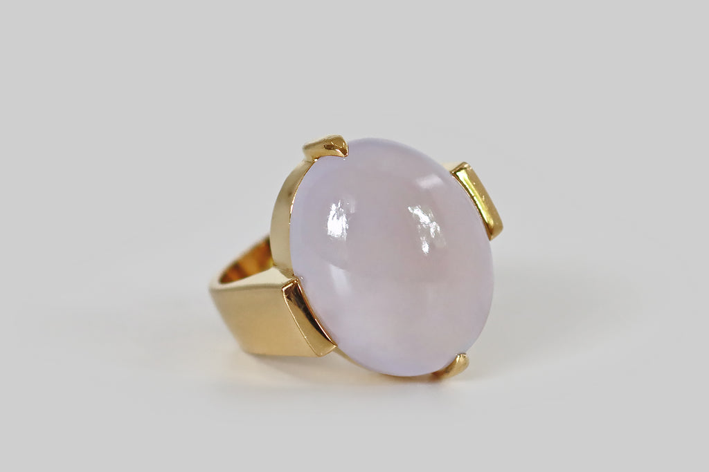 Poor Mouchette | Curated Antique Jewelry, Vintage Jewelry & Engagement Rings | A monumental late-vintage ring, modeled in 18k yellow gold, whose gem is a 28 carat, type A, lavender jade cabochon. This pale, cool lavender jade is highly translucent, with a glowing quality we usually associate with moonstone— an internal light seems to shift across the face of the jade, when the gem is moved. It is held in two large claw-like prongs, to the north and south.