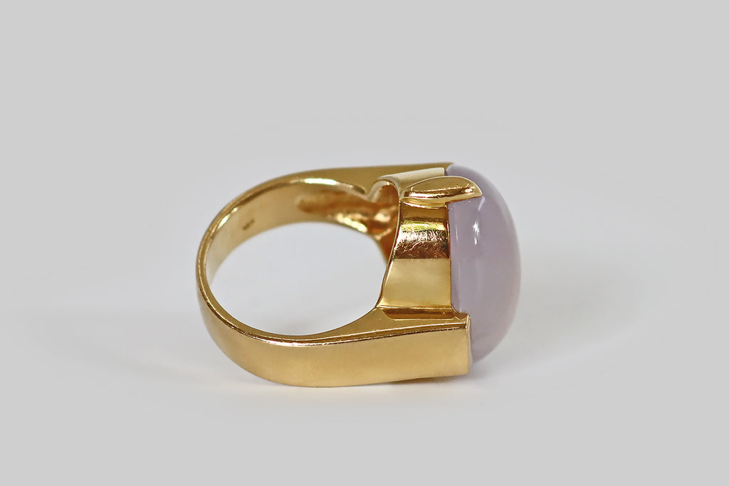 Poor Mouchette | Curated Antique Jewelry, Vintage Jewelry & Engagement Rings | A monumental late-vintage ring, modeled in 18k yellow gold, whose gem is a 28 carat, type A, lavender jade cabochon. This pale, cool lavender jade is highly translucent, with a glowing quality we usually associate with moonstone— an internal light seems to shift across the face of the jade, when the gem is moved. It is held in two large claw-like prongs, to the north and south.