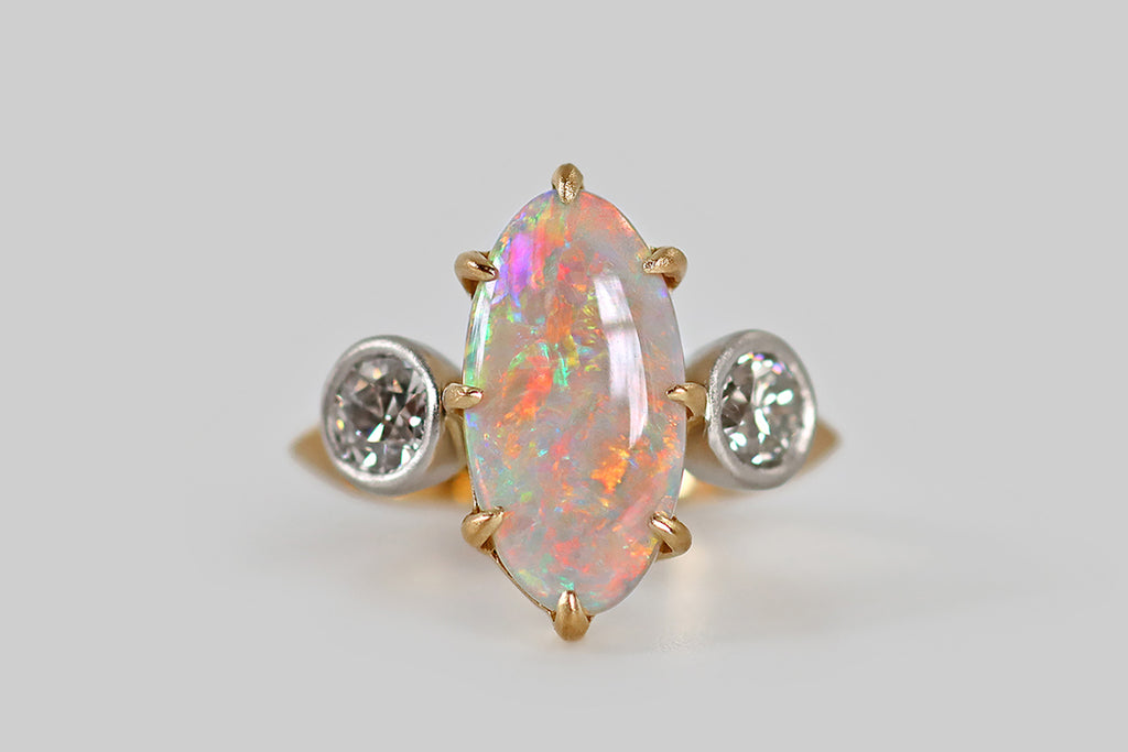Poor Mouchette | Curated Antique Jewelry, Vintage Jewelry & Engagement Rings | A striking three-stone ring, featuring an elongated, oval, Australian opal, modeled in 18k yellow gold and platinum, by your friends at Poor Mouchette. This spectacular, fiery opal is held in eight claw-like prongs<span data-mce-fragment="1">—</span> it displays a full spectrum of colors, from icy blues and greens, to highly desirable red and orange hues, to yellow and magenta.