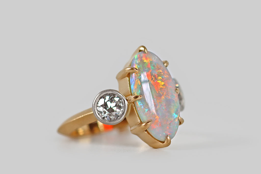 Poor Mouchette | Curated Antique Jewelry, Vintage Jewelry & Engagement Rings | A striking three-stone ring, featuring an elongated, oval, Australian opal, modeled in 18k yellow gold and platinum, by your friends at Poor Mouchette. This spectacular, fiery opal is held in eight claw-like prongs<span data-mce-fragment="1">—</span> it displays a full spectrum of colors, from icy blues and greens, to highly desirable red and orange hues, to yellow and magenta. 