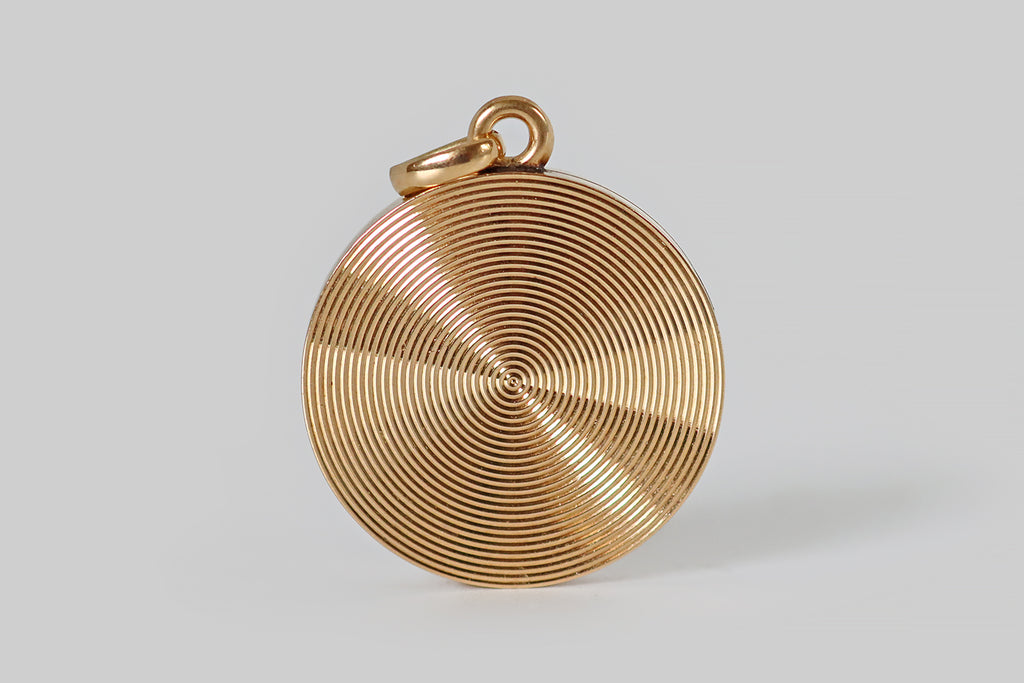 Poor Mouchette | Curated Antique Jewelry, Vintage Jewelry & Engagement Rings | Portland, Oregon |An early Art Deco era locket, modeled in 14k yellow gold, whose decor is a series of engraved, close-set, concentric circles, expanding outward from the locket's central, old European cut diamond. This locket is especially beautiful in movement, when its grooved surface reflects the light in an almost hypnotic manner! It reminds us of an LP, or of a hypnotist's wheel. We love it for this reason