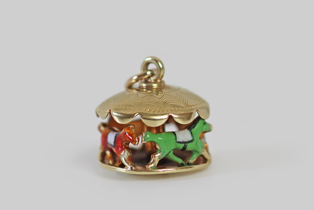 Antique Jewelry Portland, Vintage Jewelry Portland , Antique Engagement Rings | Poor Mouchette | A dainty vintage carousel charm, made in 14k yellow gold, by the well-known New York jewelers Sloan & Co. This clever little jewel depicts a series of four saddled carousel horses, arranged nose to tail, under a scalloped awning. Each of these miniature equine friends is enameled in a different color— they are green, white, tawny, and black.