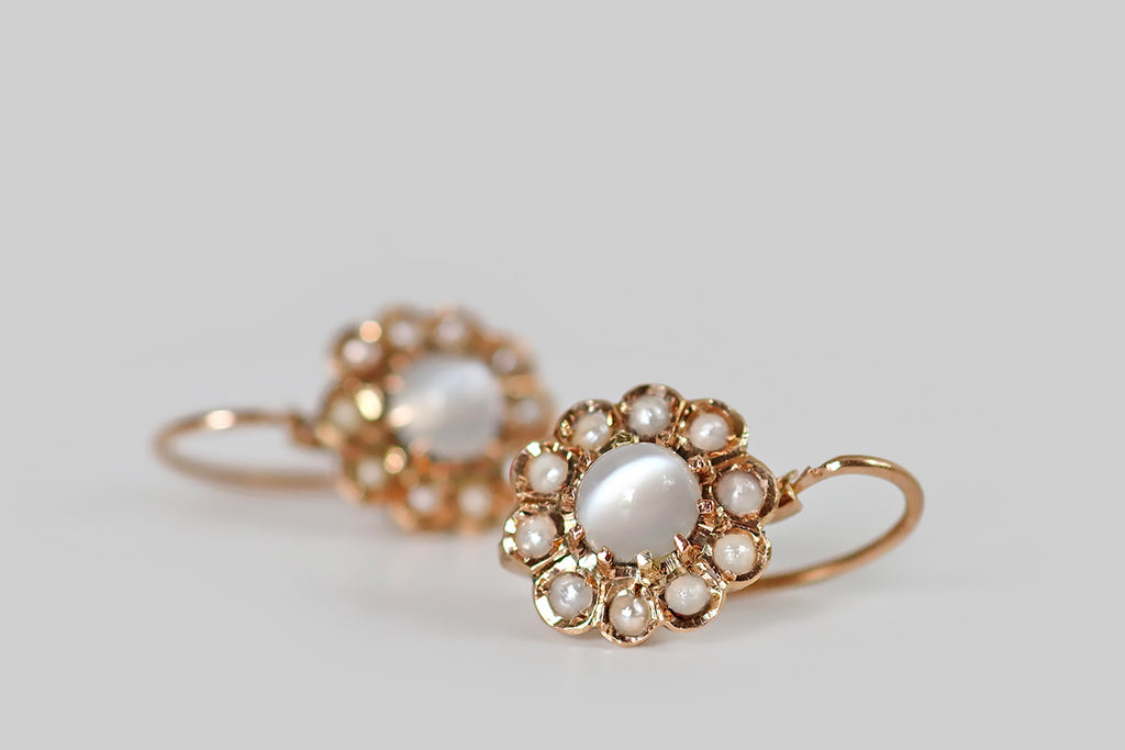 Antique Jewelry Portland, Vintage Jewelry Portland , Antique Engagement Rings | Poor Mouchette | A very sweet pair of Victorian-era, flower-form drop earrings, modeled in 14k rosy yellow gold, whose central elements are a pair of glowing, white cat's eye moonstones. These moonstones have a strong, vertical eye, that shifts across the stone-face, with movement. Each is held in ten, claw-like prongs, where it is surrounded by a bevy of "petals," each set with a small, cream-colored seed pearl.
