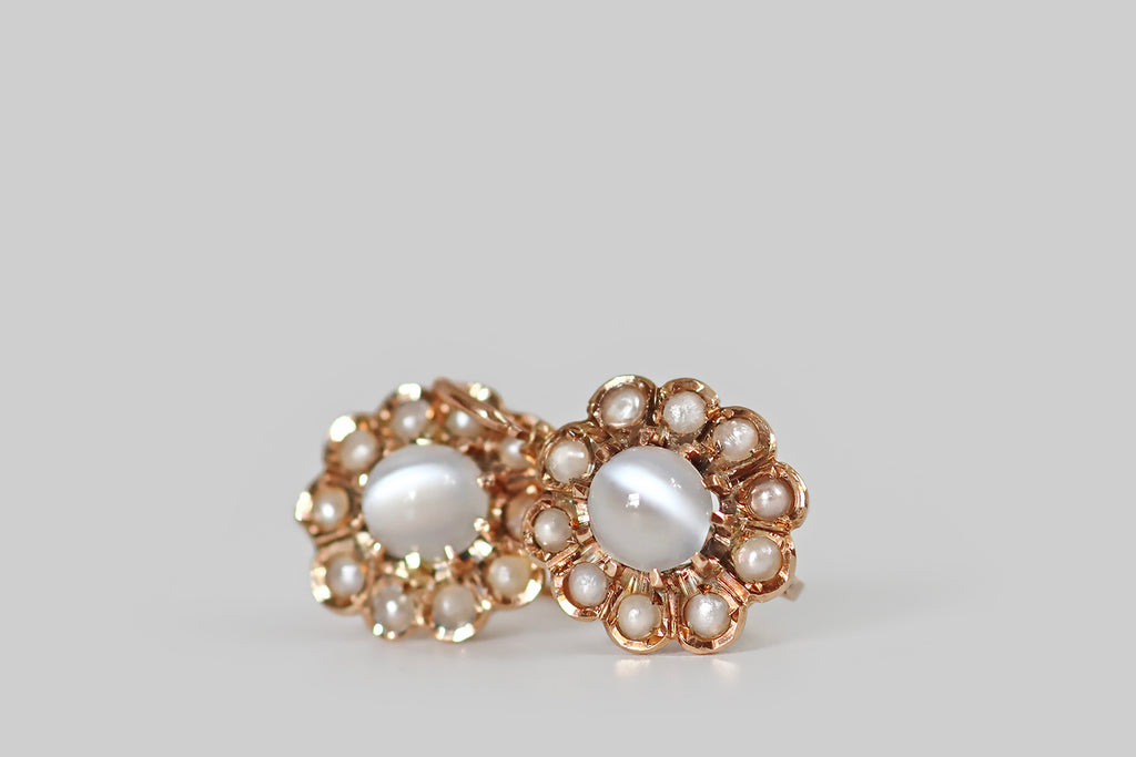 Antique Jewelry Portland, Vintage Jewelry Portland , Antique Engagement Rings | Poor Mouchette | A very sweet pair of Victorian-era, flower-form drop earrings, modeled in 14k rosy yellow gold, whose central elements are a pair of glowing, white cat's eye moonstones. These moonstones have a strong, vertical eye, that shifts across the stone-face, with movement. Each is held in ten, claw-like prongs, where it is surrounded by a bevy of "petals," each set with a small, cream-colored seed pearl.