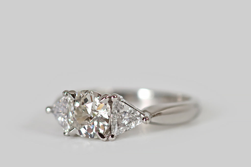 Antique Jewelry Portland, Vintage Jewelry Portland , Antique Engagement Rings | Poor Mouchette | A striking, 1940s, three-stone engagement ring, modeled in platinum, whose central, old mine cushion cut diamond is flanked by a pair of antique triangle cuts. The old mine cut diamond is vibrant, with flashing, slightly-irregular facets, a small table, and a large open culet. The antique triangles are bright and sparkly, with many, slender, ray-like facets and tiny, open culets.