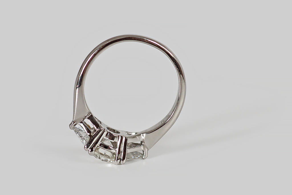 Antique Jewelry Portland, Vintage Jewelry Portland , Antique Engagement Rings | Poor Mouchette | A striking, 1940s, three-stone engagement ring, modeled in platinum, whose central, old mine cushion cut diamond is flanked by a pair of antique triangle cuts. The old mine cut diamond is vibrant, with flashing, slightly-irregular facets, a small table, and a large open culet. The antique triangles are bright and sparkly, with many, slender, ray-like facets and tiny, open culets.