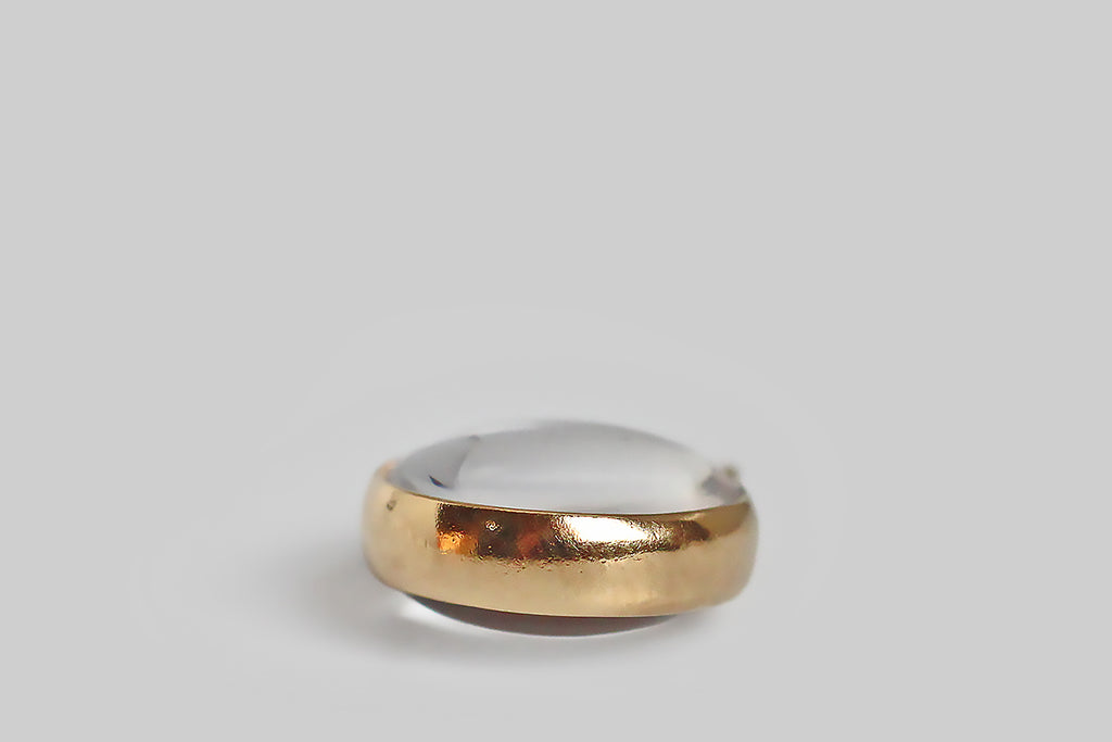  Antique Jewelry Portland, Vintage Jewelry Portland , Antique Engagement Rings | Poor Mouchette | A dainty, mid 20th century charm, whose broad 14k yellow gold bezel frames an optically clear, two-domed, crystal cabochon. This little charm is strikingly minimal— its transparent crystal reads like a drop of water, suspended inside a gold ring. It has a serene visual quality when worn alone on a slender chain. This charm was probably intended as a small magnifying glass.