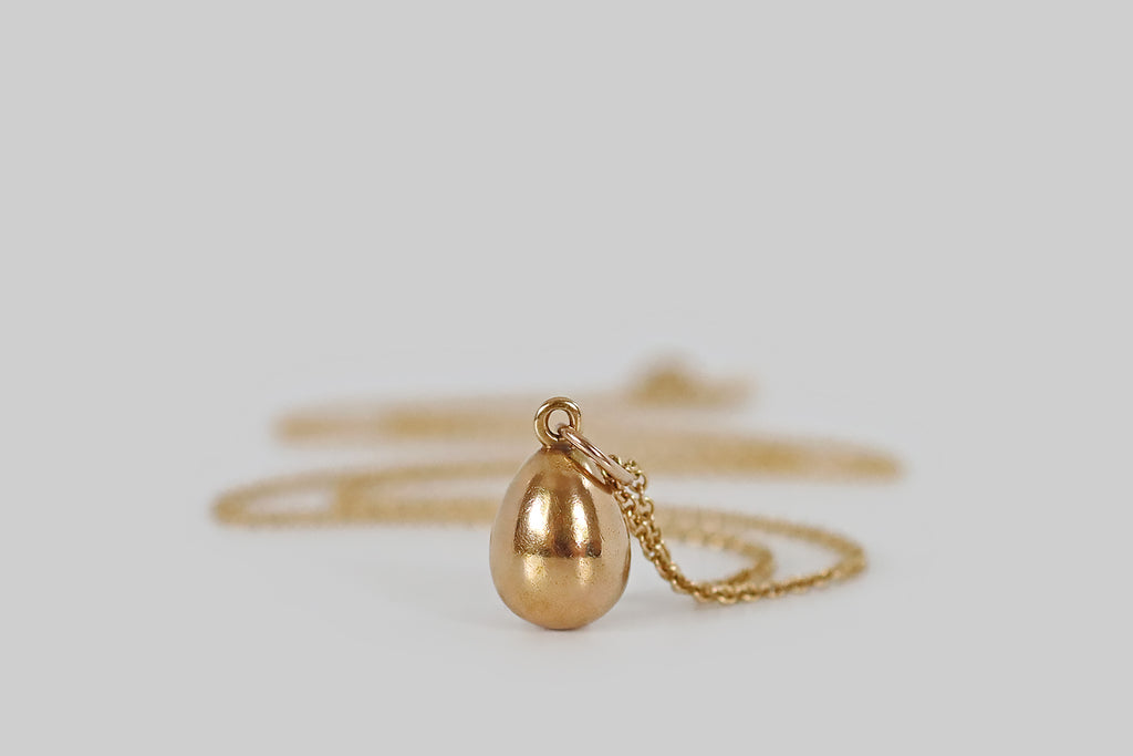 Antique Jewelry Portland, Vintage Jewelry Portland , Antique Engagement Rings | Poor Mouchette | A miniature, imperial Russian egg pendant, modeled in 14k yellow gold, whose single embellishment is a peaked, oval, medium-blue, natural, sapphire cabochon. This glowing, sugarloaf sapphire nests in the face of our little egg, where it is secured by the low profile edge of its seat, and a pair of graved beads.