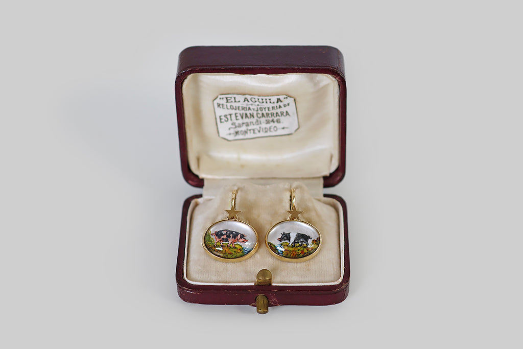 Poor Mouchette | Curated Antique Jewelry, Vintage Jewelry & Engagement Rings | Portland, Oregon | A very cool pair of drop earrings, modeled in 18k yellow gold, whose "gems" are a pair of reverse-carved, high-dome crystals. These wonderful miniatures have been finely hand-carved and painted with the realistic likenesses of two pigs— one pink with black spots (a Gloucestershire Old Spots), and one black with a white swath across its shoulders (a British Saddleback).