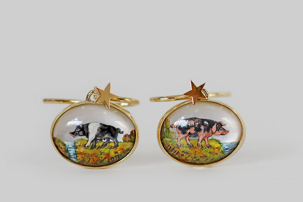 Poor Mouchette | Curated Antique Jewelry, Vintage Jewelry & Engagement Rings | Portland, Oregon | A very cool pair of drop earrings, modeled in 18k yellow gold, whose "gems" are a pair of reverse-carved, high-dome crystals. These wonderful miniatures have been finely hand-carved and painted with the realistic likenesses of two pigs— one pink with black spots (a Gloucestershire Old Spots), and one black with a white swath across its shoulders (a British Saddleback).