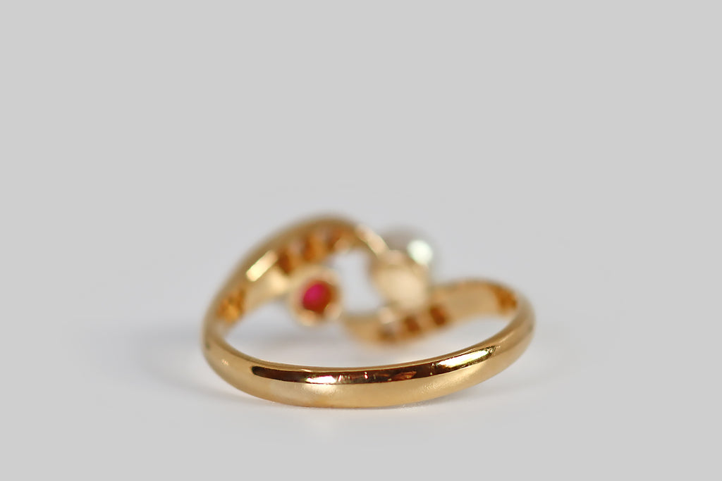 Poor Mouchette | Curated Antique Jewelry, Vintage Jewelry & Engagement Rings | Portland, Oregon | A charming, early-20th-century engagement ring, modeled in 18k yellow gold, whose form is a modified (open) bypass, where each tapering, diamond-set "ribbon" terminates in a gemstone finial. These primary gems are a highly-saturated, bright-red, old cut ruby (set in eight prongs), and a luminous white sea-pearl.