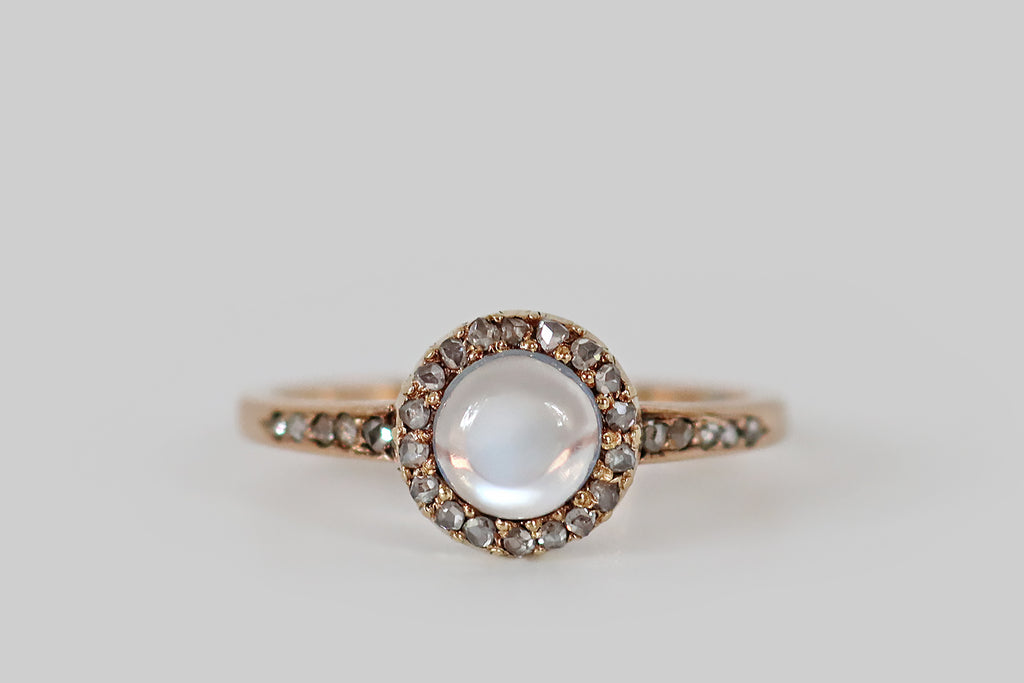 Antique Jewelry Portland, Vintage Jewelry Portland , Antique Engagement Rings | Poor Mouchette | An early twentieth century ring, modeled in 14k rose gold, whose primary gem is a round, blue-flash moonstone cabochon. This moonstone is held in a nest of eighteen bead-like prongs, where it is surrounded by a halo of eighteen silvery rose cut diamonds. These tiny rose cuts share prongs with the moonstone, and they are further secured by the ring's crimped outer bezel. 