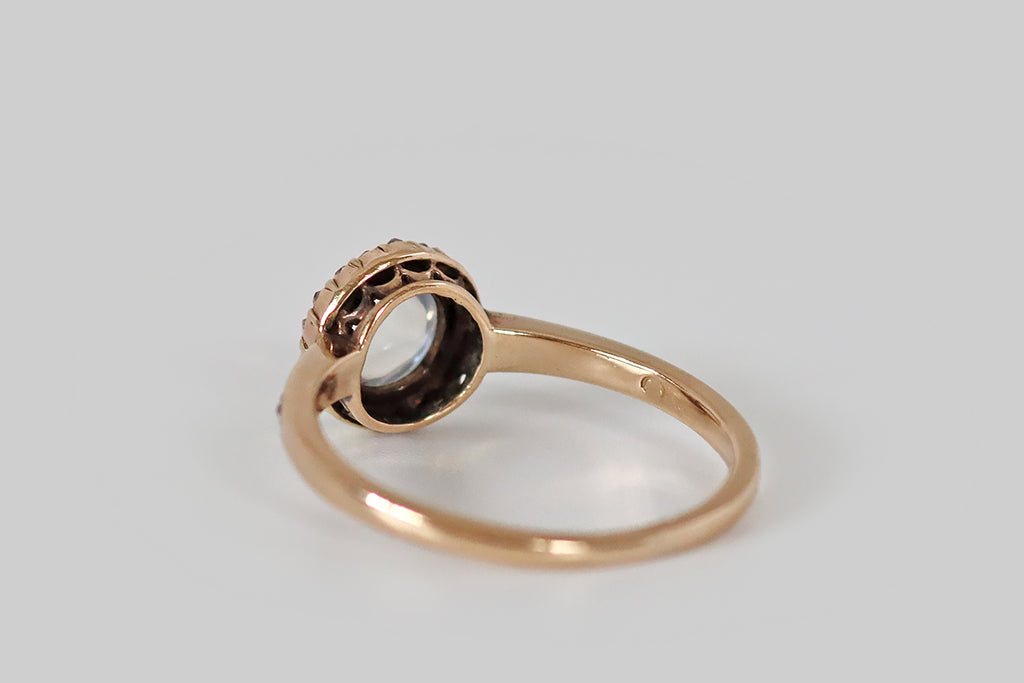 Antique Jewelry Portland, Vintage Jewelry Portland , Antique Engagement Rings | Poor Mouchette | An early twentieth century ring, modeled in 14k rose gold, whose primary gem is a round, blue-flash moonstone cabochon. This moonstone is held in a nest of eighteen bead-like prongs, where it is surrounded by a halo of eighteen silvery rose cut diamonds. These tiny rose cuts share prongs with the moonstone, and they are further secured by the ring's crimped outer bezel. 