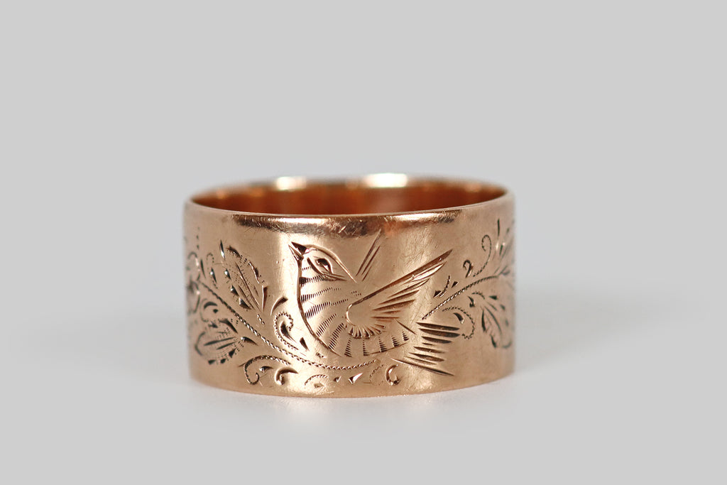Antique Jewelry Portland, Vintage Jewelry Portland , Antique Engagement Rings | Poor Mouchette | An extra-wide Victorian era cigar band ring, fabricated in 10k rose gold and hand-engraved with a beautiful sparrow. This sparrow is captured, mid-song, perched amid sprays of foliage and charming five-petaled flowers. The long, expressive strokes that define our bird friend's wings and tail, animating him by implying movement