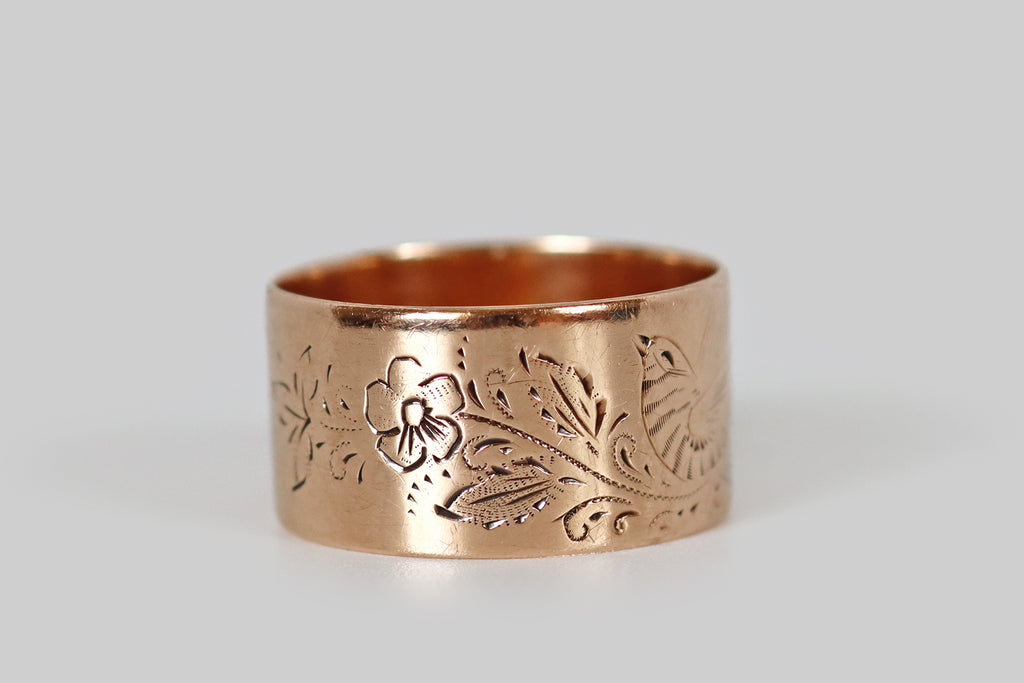 Antique Jewelry Portland, Vintage Jewelry Portland , Antique Engagement Rings | Poor Mouchette | An extra-wide Victorian era cigar band ring, fabricated in 10k rose gold and hand-engraved with a beautiful sparrow. This sparrow is captured, mid-song, perched amid sprays of foliage and charming five-petaled flowers. The long, expressive strokes that define our bird friend's wings and tail, animating him by implying movement