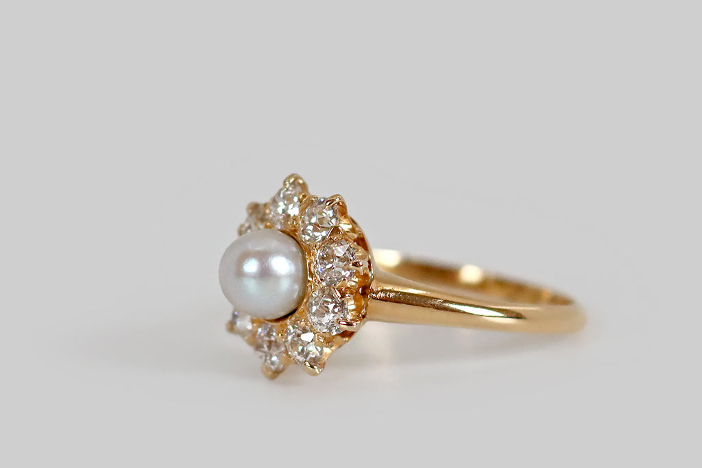 Poor Mouchette | Curated Antique Jewelry, Vintage Jewelry & Engagement Rings | A sweet Victorian-era ring, modeled in 18k yellow gold, whose central gem is a luminous, natural, saltwater pearl. Surrounding this pearl, a series of nine old European cut diamonds (H/I, VS1-SI1) rest in a combination of fishtails and claw-like prongs. This ring has a pierced, crown-like gallery.