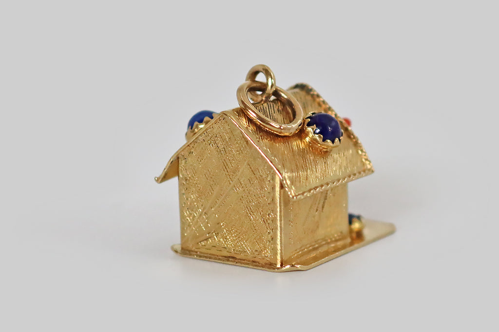 Antique Jewelry Portland, Vintage Jewelry Portland , Antique Engagement Rings | Poor Mouchette |A large, mid twentieth century charm, fabricated in 18k yellow gold, resembling a classic doghouse with a pup inside! Our faithful doggo was hand-carved from vibrant Sardinian coral, and the carver has positioned a naturally-occurring white spot in the middle of his forehead. He sits inside the doorway of his gold house, wearing a twisted gold tie out— beside him, a water bowl (a lapis lazuli cabochon.