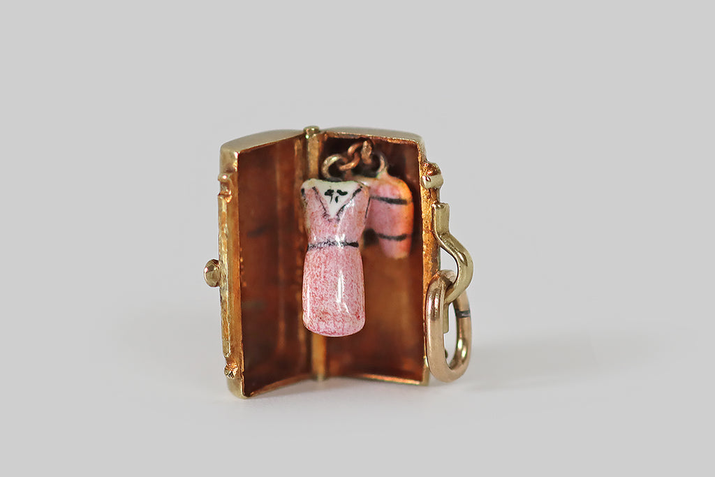 Antique Jewelry Portland, Vintage Jewelry Portland , Antique Engagement Rings | Poor Mouchette | A dainty, vintage charm, modeled as a weekend bag, by the well-known makers Sloan & Co., in 14k yellow gold. This get-away bag opens to reveal a puffy dress and bloomers, hanging inside— the miniature frock is enameled in pink and white, with black piping and a tiny black floral detail at the neck, and the little bloomers are made to match!