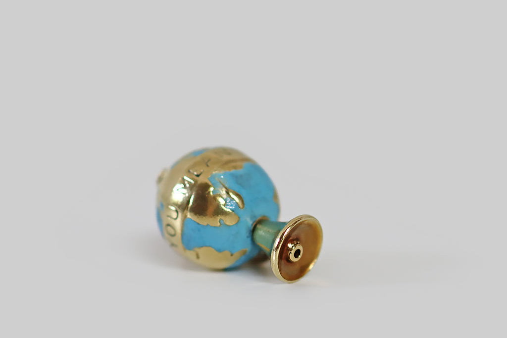 Antique Jewelry Portland, Vintage Jewelry Portland , Antique Engagement Rings | Poor Mouchette | A rare and wonderful vintage charm, modeled in 14k gold, as a spinning globe, on a footed stand. This little globe is beautiful and highly detailed! Here, the earth's land masses are rendered in polished gold, while the seas are a field of bright blue enamel. A gold banner, bearing the sentiment "you mean the world to me" encircles the globe, like a horizon band.