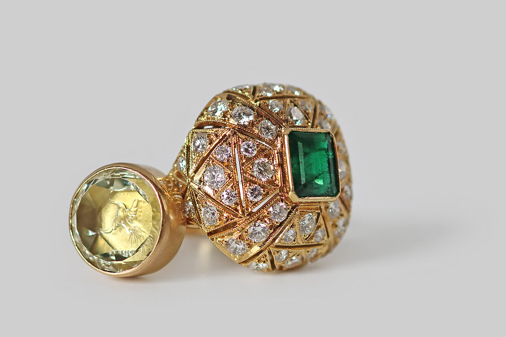 Antique Jewelry Portland, Vintage Jewelry Portland , Antique Engagement Rings | Poor Mouchette | A glamorous, mid-twentieth-century ring, modeled in 18k yellow gold, whose cushion-shaped face is encrusted with an ornate arrangement of gemstones— many, sparkling round brilliant cut diamonds, surrounding a central, rich-green, step-cut emerald.&nbsp;This ring has a soft, bombe-like profile. The emerald rests at the center of the ring face