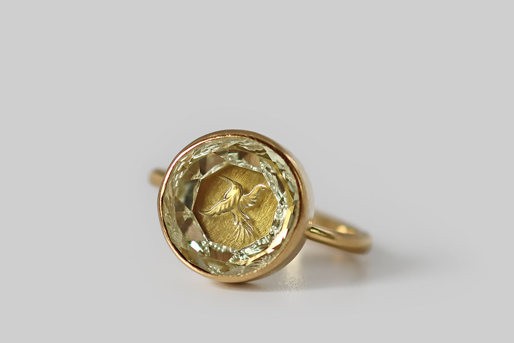 Antique Jewelry Portland, Vintage Jewelry Portland , Antique Engagement Rings | Poor Mouchette | A striking contemporary ring, modeled in 18k yellow gold, by the designer&nbsp;Annette Ferdinandsen. This signet-style ring features a carved yellow beryl gem, whose intaglio subject is a tiny hummingbird in flight— this is a reverse carving, so the little bird is carved on the underside of the stone, where he stands out against the brushed, high-color surface of the ring's closed back setting. 