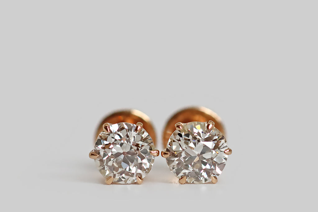 Poor Mouchette | Curated Antique Jewelry, Vintage Jewelry & Engagement Rings | Portland, Oregon | A special pair of antique diamond stud earrings, whose soulful, early, old European cut diamonds are held in six prong mounts. These elegant, 14k rose gold mounts are crown-like with deeply cutaway sides. Their prongs are tapering and claw-like; their posts are threaded, for security, and the precisely-made nuts are fashioned with a clever, crescent-shaped stirrup.