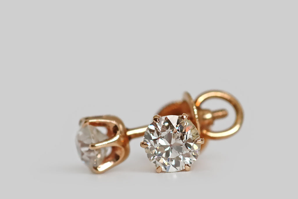 Poor Mouchette | Curated Antique Jewelry, Vintage Jewelry & Engagement Rings | Portland, Oregon | A special pair of antique diamond stud earrings, whose soulful, early, old European cut diamonds are held in six prong mounts. These elegant, 14k rose gold mounts are crown-like with deeply cutaway sides. Their prongs are tapering and claw-like; their posts are threaded, for security, and the precisely-made nuts are fashioned with a clever, crescent-shaped stirrup.