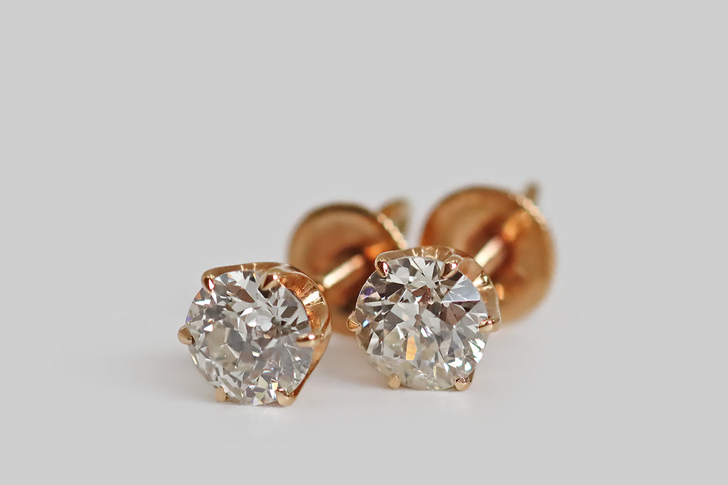 Poor Mouchette | Curated Antique Jewelry, Vintage Jewelry & Engagement Rings | Portland, Oregon | A special pair of antique diamond stud earrings, whose soulful, early, old European cut diamonds are held in six prong mounts. These elegant, 14k rose gold mounts are crown-like with deeply cutaway sides. Their prongs are tapering and claw-like; their posts are threaded, for security, and the precisely-made nuts are fashioned with a clever, crescent-shaped stirrup.