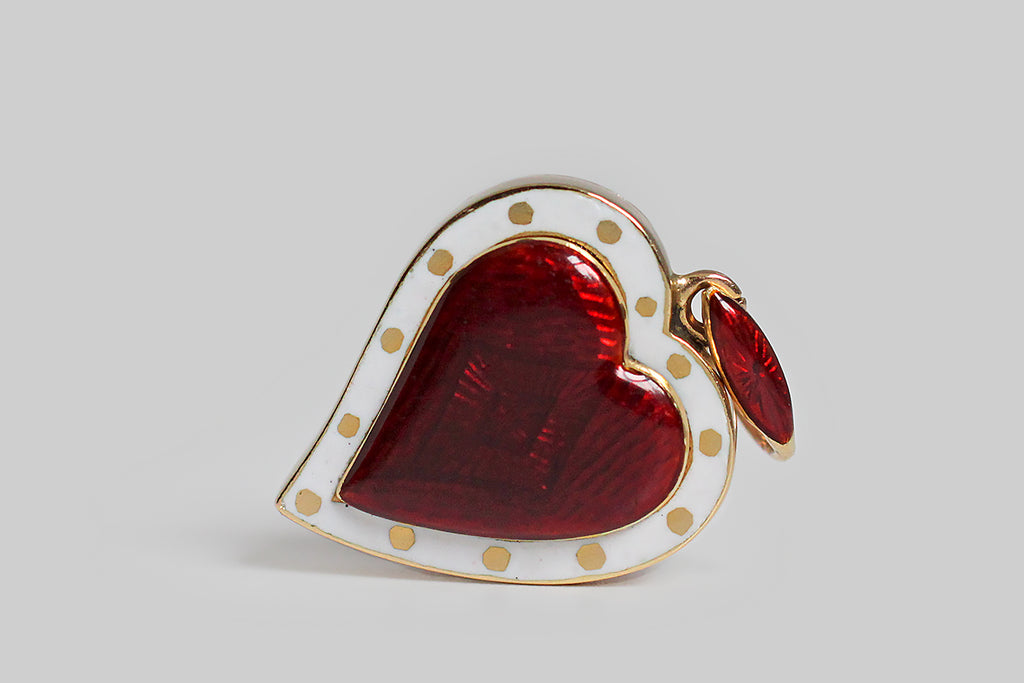 A Victorian-era witch’s heart locket, beautifully made in 15k gold, and attributed to the jewelers Child & Child. Our bewitched heart’s glossy, red, guilloche enamel center features a subtle diamond shaped guilloche pattern. It is encircled by a slim band of white enamel, and this border is decorated with charming gold polka dots. The heart’s reverse has a lift-out, glazed, locket compartment, meant to hold a lock of hair, a photograph, or another small ephemeral object. 