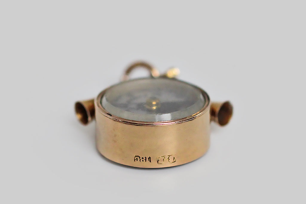 An unusual, Victorian-era, working, compass watch fob, modeled in 18k rosy yellow gold, and crowned with a sleek pair of hunt horns and a small horseshoe. The compass face is silvery, with black markings to indicate the cardinal and inter-cardinal directions; the words "true north" are printed alongside the needle that indicates North. 