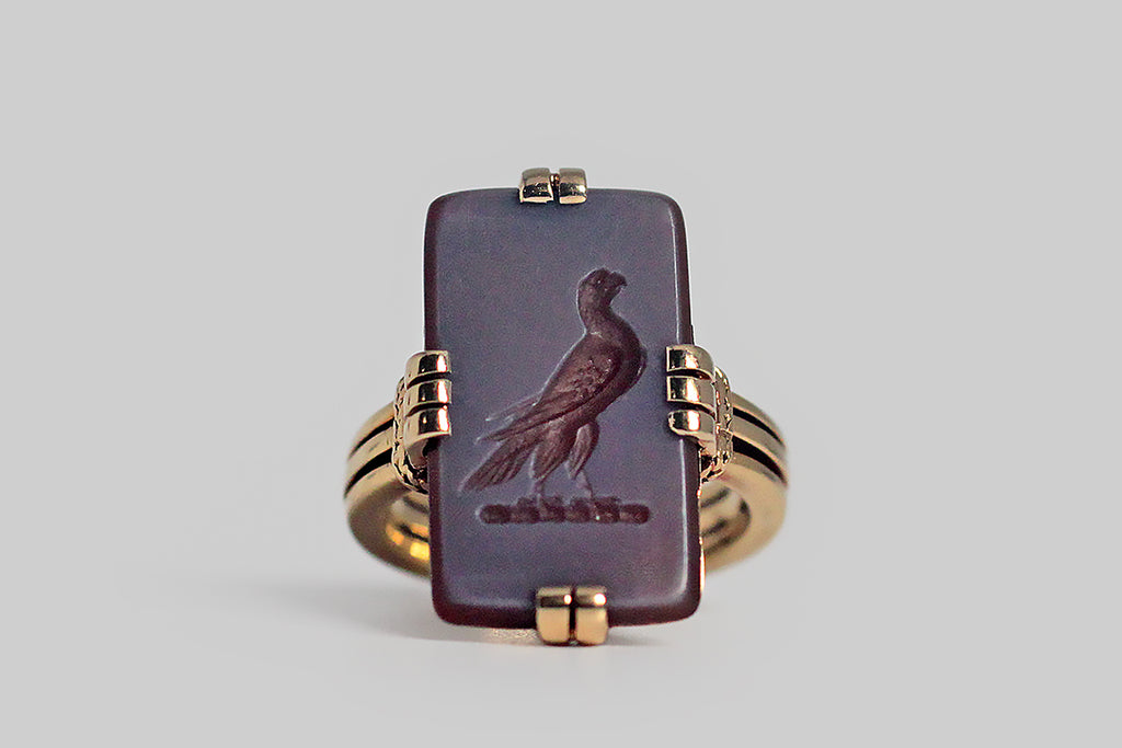 A turn-of-the-century (20th) intaglio ring of rare quality, made in 18k yellow gold and featuring the most beautiful, finely-detailed, hardstone carving of a falcon. This romantic figure is hand carved into a rectangular sard slab (sard is an earthy-red variety of chalcedony). He is very dignified, with his breast thrust forward. The hook in his beak is crisp and clear, as are the tiny feathers of his wings. This rectangular gem is held securely in squared groups of prongs