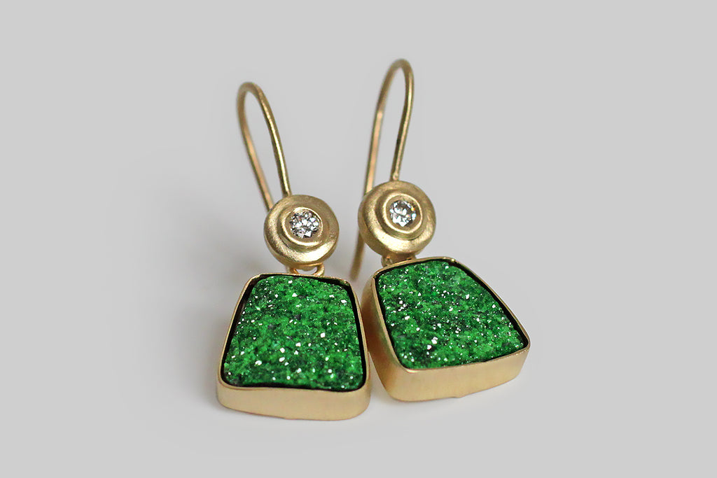 Vibrant-green, trapezoidal slabs of Uvarovite garnet druzy dangle beneath a bright pair of brilliant-cut white diamonds. These diamonds are mounted in an exaggerated bezel, which is circular and subtly organic in form. The Uvarovite garnet druzy slabs are held in full, closed-back bezels— they are a spectacular shade of green, unique to this rarest variety of garnet, and they sparkle like mad! Metal is all 18k