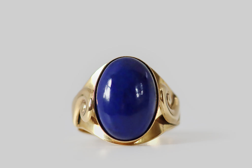 Antique Jewelry Portland, Vintage Jewelry Portland , Antique Engagement Rings | Poor Mouchette | A striking, late-century, Italian, lapis lazuli ring, modeled in 14k yellow gold, whose shoulders are decorated with a pair of voluptuous spirals. These spiral forms are "lifted" off the ring shank— they have soft, curved edges, and they terminate in a series of wing-like bars or hashes. 