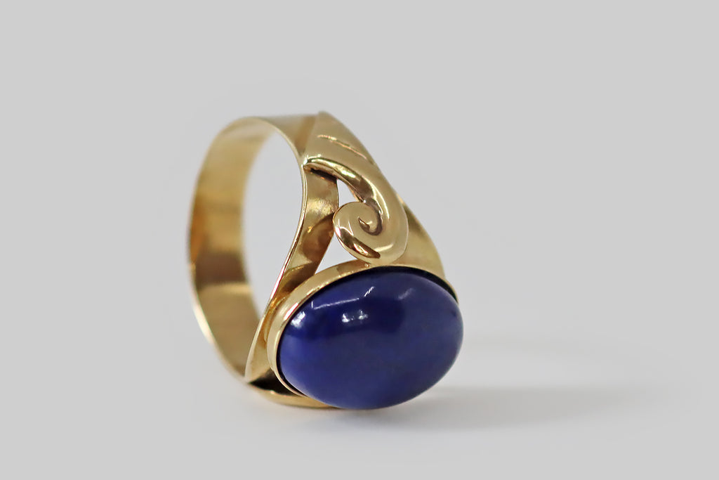 Antique Jewelry Portland, Vintage Jewelry Portland , Antique Engagement Rings | Poor Mouchette | A striking, late-century, Italian, lapis lazuli ring, modeled in 14k yellow gold, whose shoulders are decorated with a pair of voluptuous spirals. These spiral forms are "lifted" off the ring shank— they have soft, curved edges, and they terminate in a series of wing-like bars or hashes.