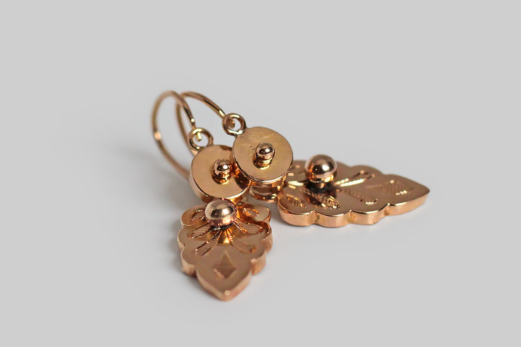 A dainty pair of antique, 18k rose gold, day and night earrings, whose drops are modeled as shapely leaves, most closely resembling the leaves of the Swedish White Beam tree. These feather-weight, French-made earrings have small, round, dormeuse-style tops, with back-to-front threading, hinged earwires. Their delicate, hand-engraved, leaf-form drops 