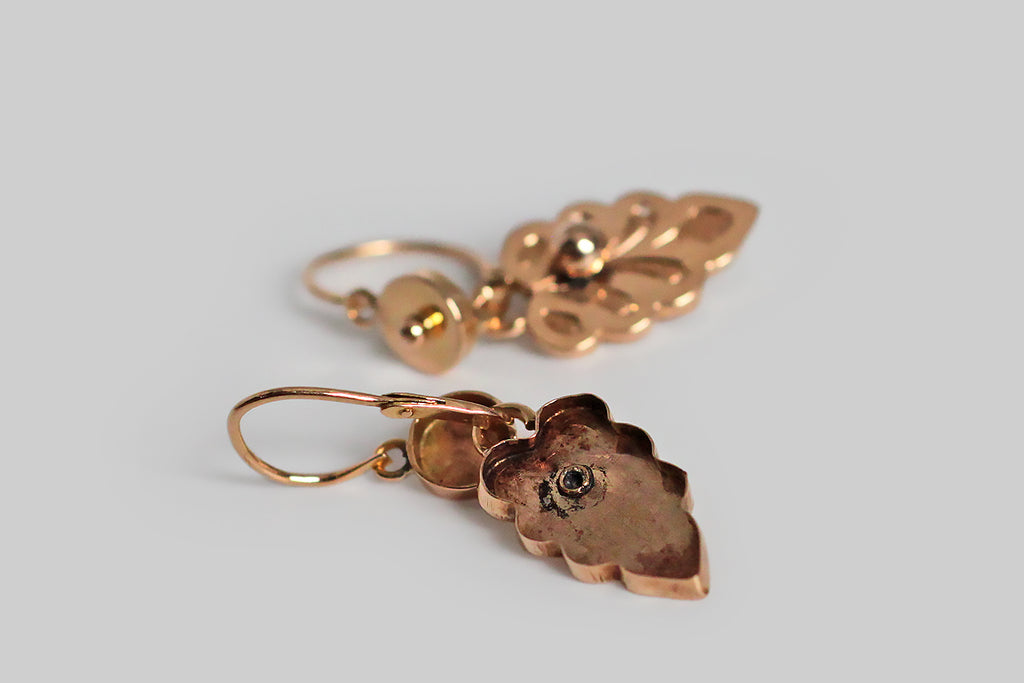 A dainty pair of antique, 18k rose gold, day and night earrings, whose drops are modeled as shapely leaves, most closely resembling the leaves of the Swedish White Beam tree. These feather-weight, French-made earrings have small, round, dormeuse-style tops, with back-to-front threading, hinged earwires. Their delicate, hand-engraved, leaf-form drops