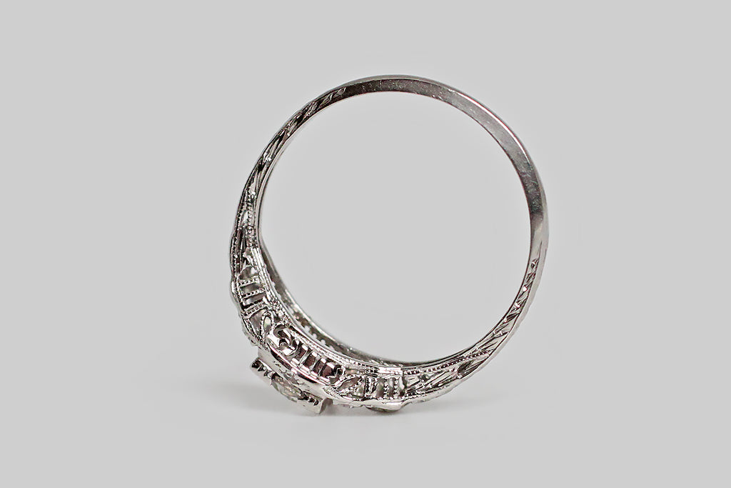 Poor Mouchette | Curated Antique Jewelry, Vintage Jewelry & Engagement Rings | Portland, Oregon | An elegant, 1930s engagement ring, modeled in platinum, whose primary gem is a 1/2 carat old European cut diamond (F/G, VS). This sparkling, hand-cut sweetheart is mounted in a low-profile, four-tab basket setting, whose "picture corner" style tabs are embellished with fine milgrain, and clover-like trios of beads. The ring head rests atop the delicate, shapely face, surrounded by pave-set, single-cut diamonds