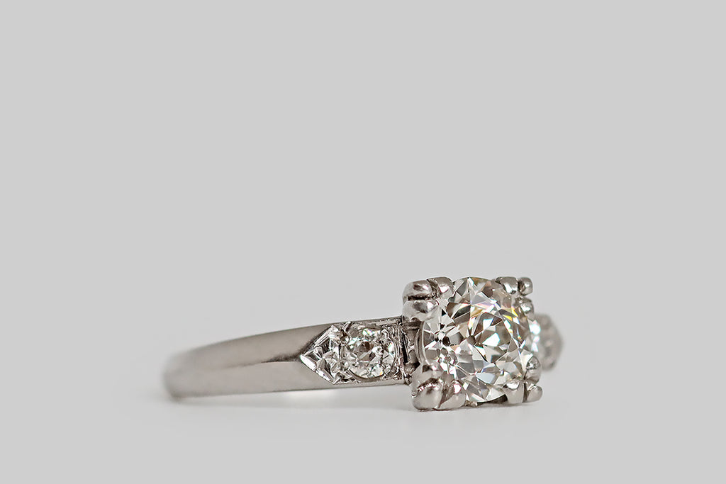 Poor Mouchette | Curated Antique Jewelry, Vintage Jewelry & Engagement Rings | Portland, Oregon | A lovely Art Deco era engagement ring, modeled in platinum, whose primary gem is a .69 carat old European cut diamond (GIA certified J/VS1). This vibrant, hand cut diamond is mounted in a low-profile basket setting, where four, clover-like, three-lobed prongs hold it securely in place. A pair of smaller, chunky, old-cut diamonds decorate the ring's shoulders, where they are bead-set into pennant-shaped seats.